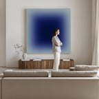A woman stands in a minimalist living room, her arms crossed, with a large blue abstract painting on the wall behind her.