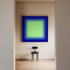 May include: A square wall art piece featuring a vibrant lime green center that fades into a deep royal blue border, framed in a thin light wood. Below the artwork sits a small, black, three-legged stool with a rectangular backrest.