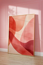 May include: Abstract art print with a gold frame. The print features a design of overlapping, organic shapes in shades of pink, red, and orange. The print is displayed against a pink wall.