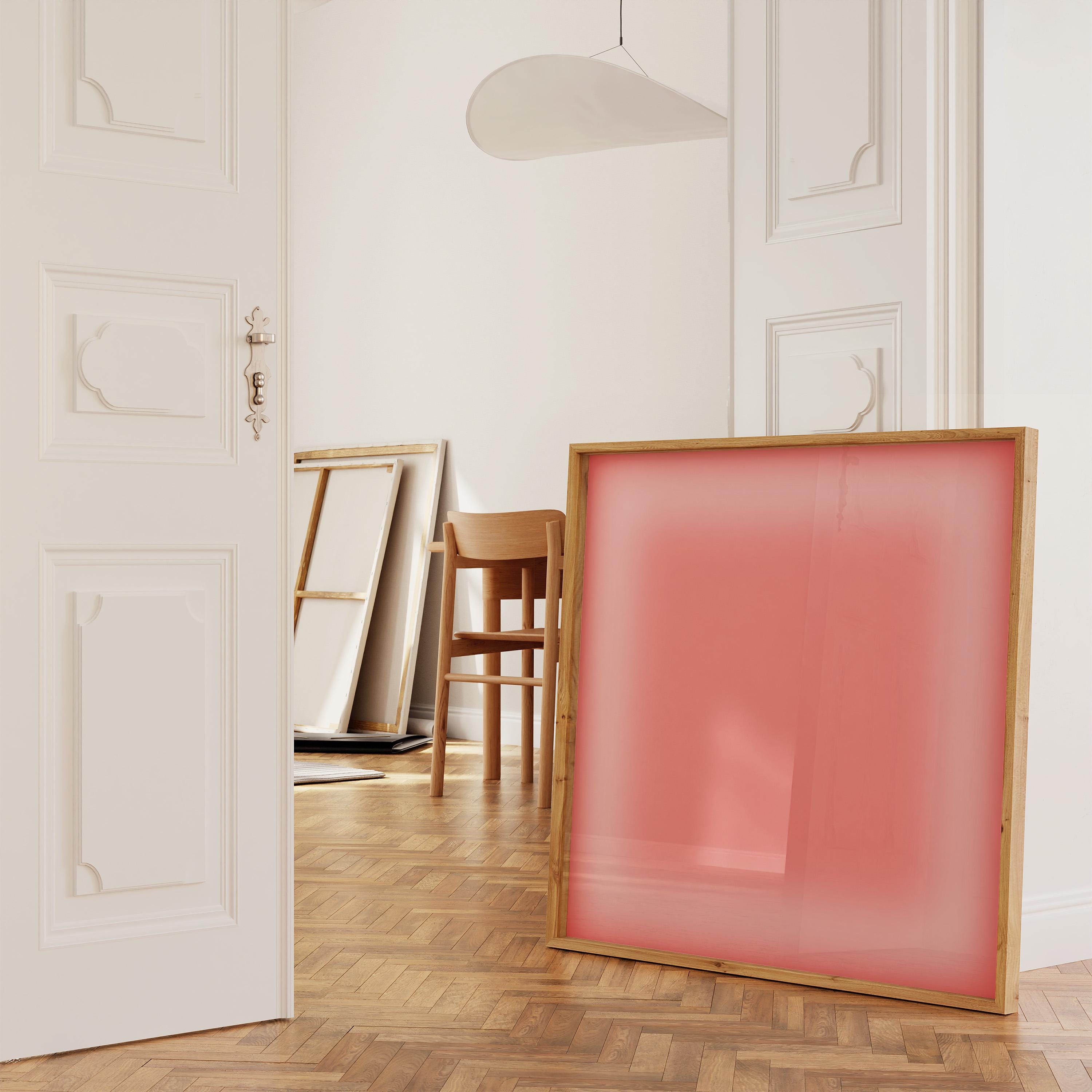 May include: A large, square artwork with a light pink translucent panel is set in a natural wood frame. The artwork leans against a white wall in a room with a wooden floor. Other artworks and a wooden chair are also visible.