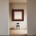 May include: An interior shot featuring a minimalist aesthetic. A black chair sits on a wooden floor beneath a large abstract painting with a brown and white gradient. The room is framed by neutral-colored walls and doorways.