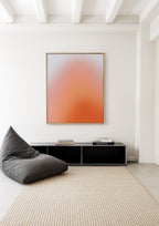 May include: A modern living room scene featuring a large abstract art piece with a gradient of orange and white tones in a gold frame. A dark gray beanbag chair sits on a beige rug, with a black cabinet and books below the artwork.