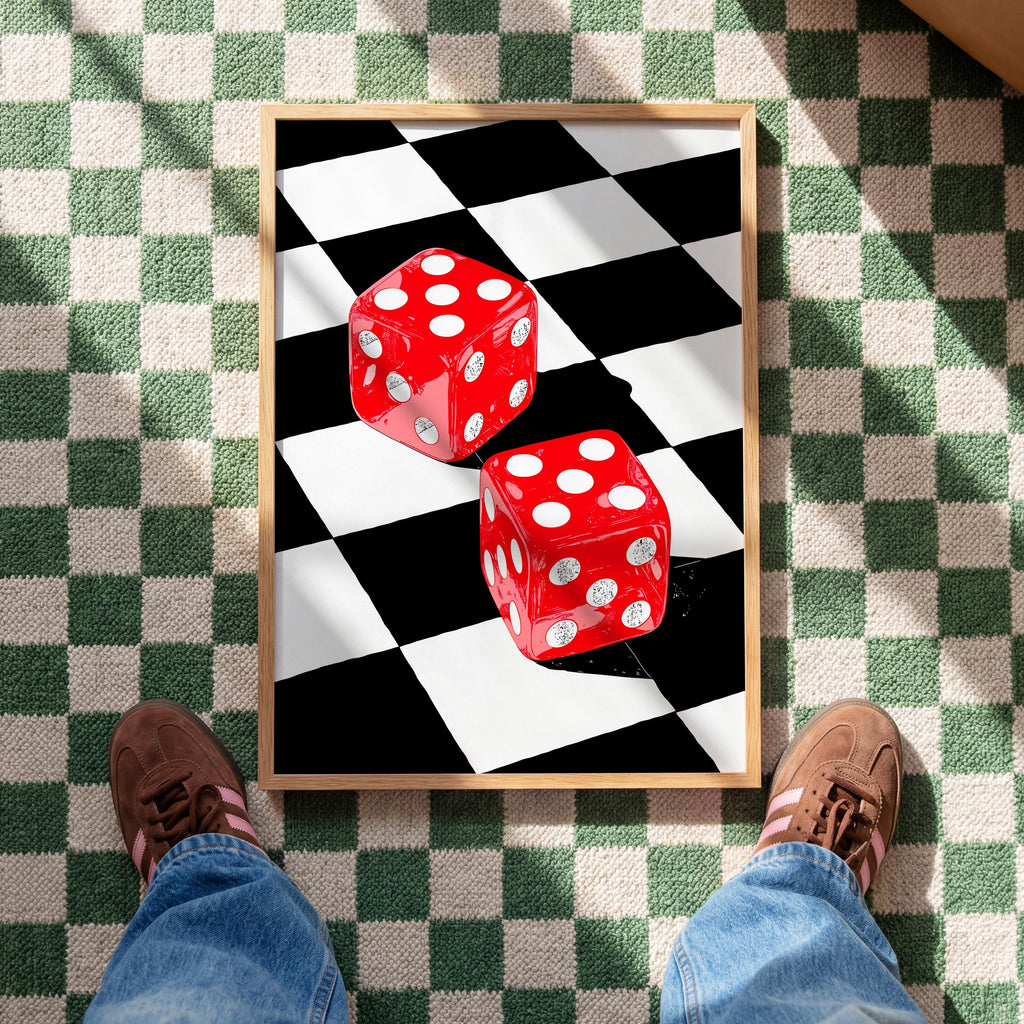 May include: A framed print featuring two red dice with white dots, set against a black and white checkered background. The dice are positioned on a diagonal, creating a dynamic composition. The frame is a light brown color.