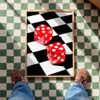May include: A framed print featuring two red dice with white dots, set against a black and white checkered background. The dice are positioned on a diagonal, creating a dynamic composition. The frame is a light brown color.