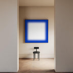 May include: A modern interior featuring a large square artwork with a vibrant blue border and a white center. Below, a small black chair stands on a wooden floor, creating a minimalist aesthetic. The room is bathed in soft, natural light.