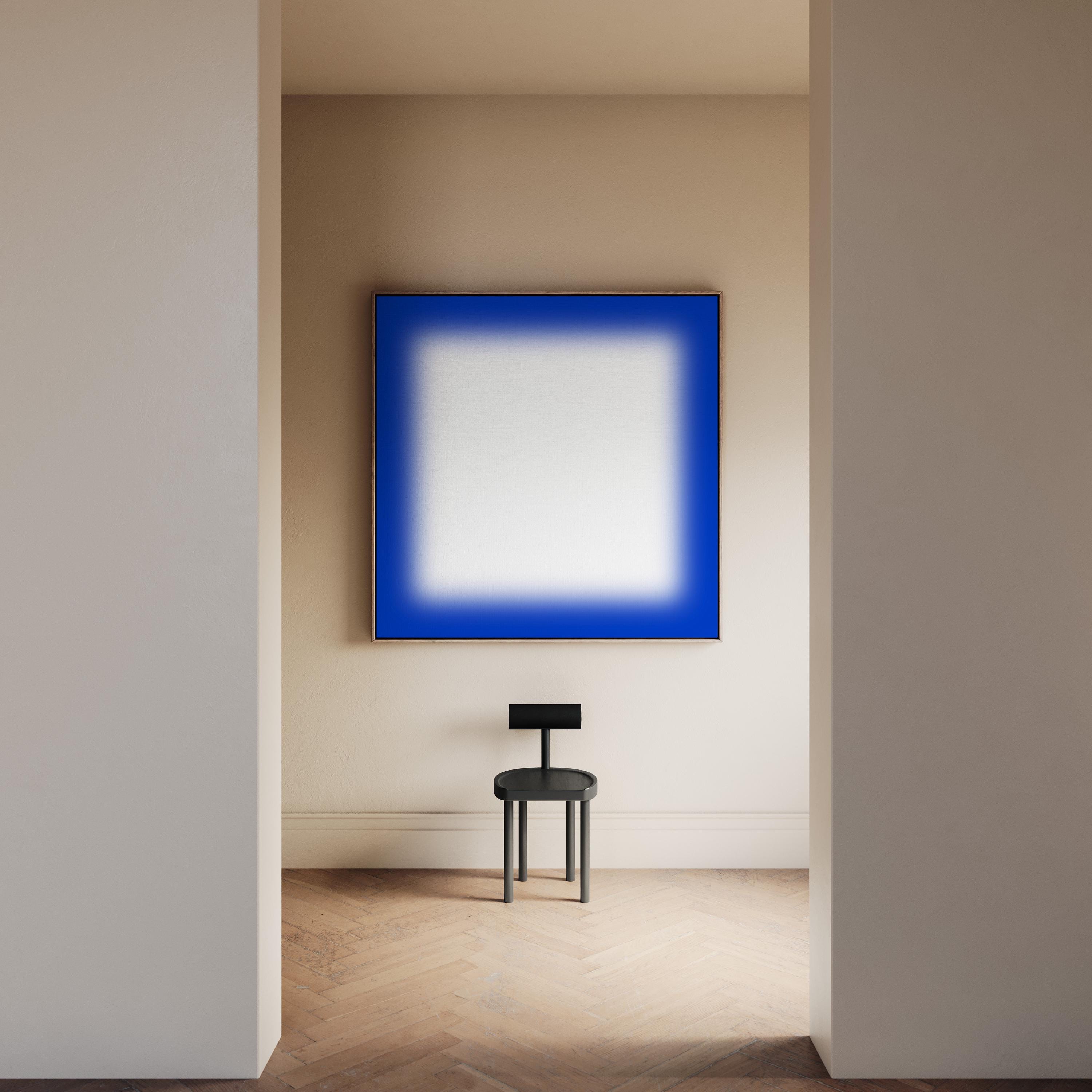 May include: A modern interior featuring a large square artwork with a vibrant blue border and a white center. Below, a small black chair stands on a wooden floor, creating a minimalist aesthetic. The room is bathed in soft, natural light.