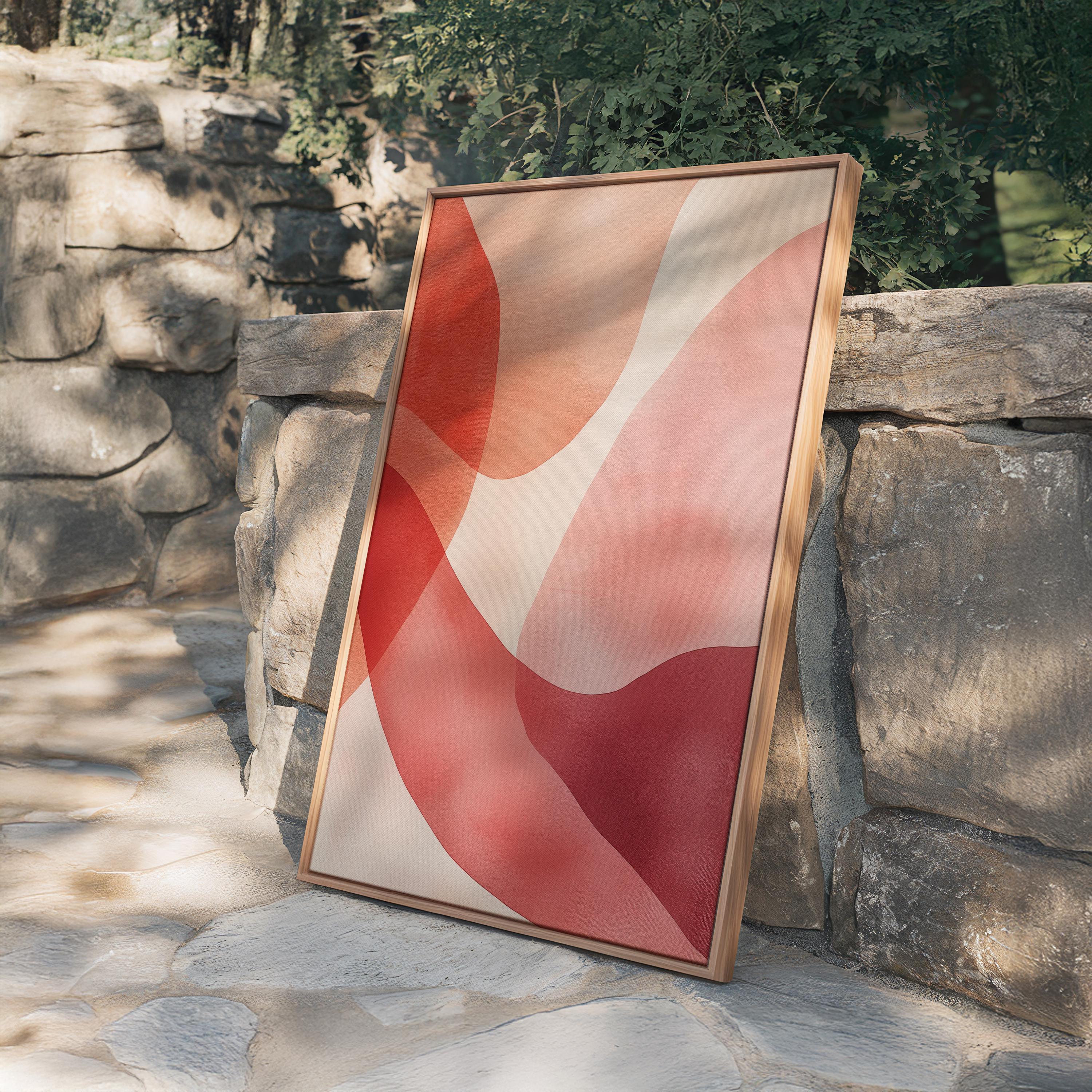 May include: A framed abstract art piece featuring overlapping shapes in shades of red, pink, and beige. The artwork has a wooden frame and leans against a stone wall, creating a modern and minimalist aesthetic.