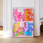 May include: A framed art print featuring four colorful gummy bear illustrations. The bears are in shades of pink, orange, yellow, and blue, with a glossy, translucent appearance. The artwork is displayed in a gold frame, leaning against a white wall.