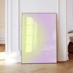 May include: A framed artwork with a gradient of yellow to purple hues. The artwork is displayed in a room with white walls and a wooden floor. The frame is a thin, warm brown color.