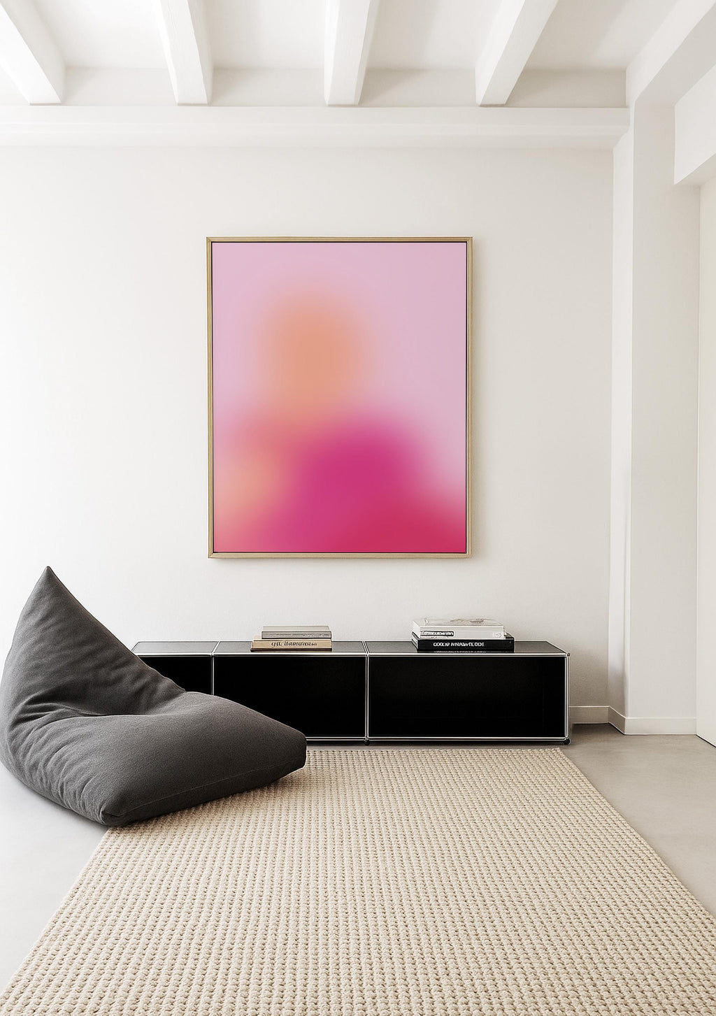 May include: A modern interior scene featuring a large abstract art piece with a pink and orange gradient, framed in gold. Below, a black cabinet and a gray beanbag chair sit on a beige rug, creating a minimalist aesthetic.