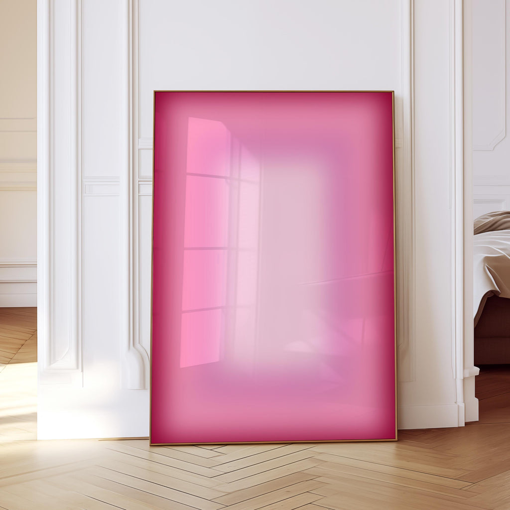May include: A framed artwork with a gradient of pink hues, from deep rose to a lighter shade. The frame is a thin, gold color. The artwork is leaning against a white wall and a wooden floor.