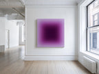 May include: A square abstract painting with a gradient of purple hues, from a deep center to a lighter surrounding. The artwork hangs on a white wall in a room with hardwood floors and a large window. The room is brightly lit.