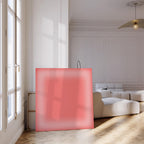 May include: A large, square, coral-colored canvas leans against a wall in a bright, modern room. The canvas has a soft, diffused gradient effect. The room features a white sofa, a large window, and a wooden floor.