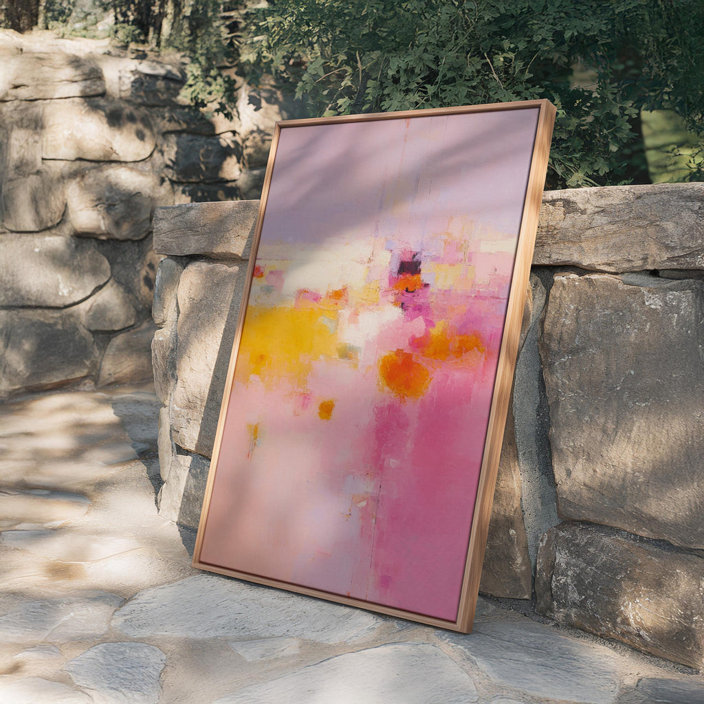 May include: Abstract art print in a wooden frame. The artwork features a blend of pink, yellow, and orange hues, creating a vibrant and energetic composition. The painting is leaning against a stone wall, showcasing its colors and textures.