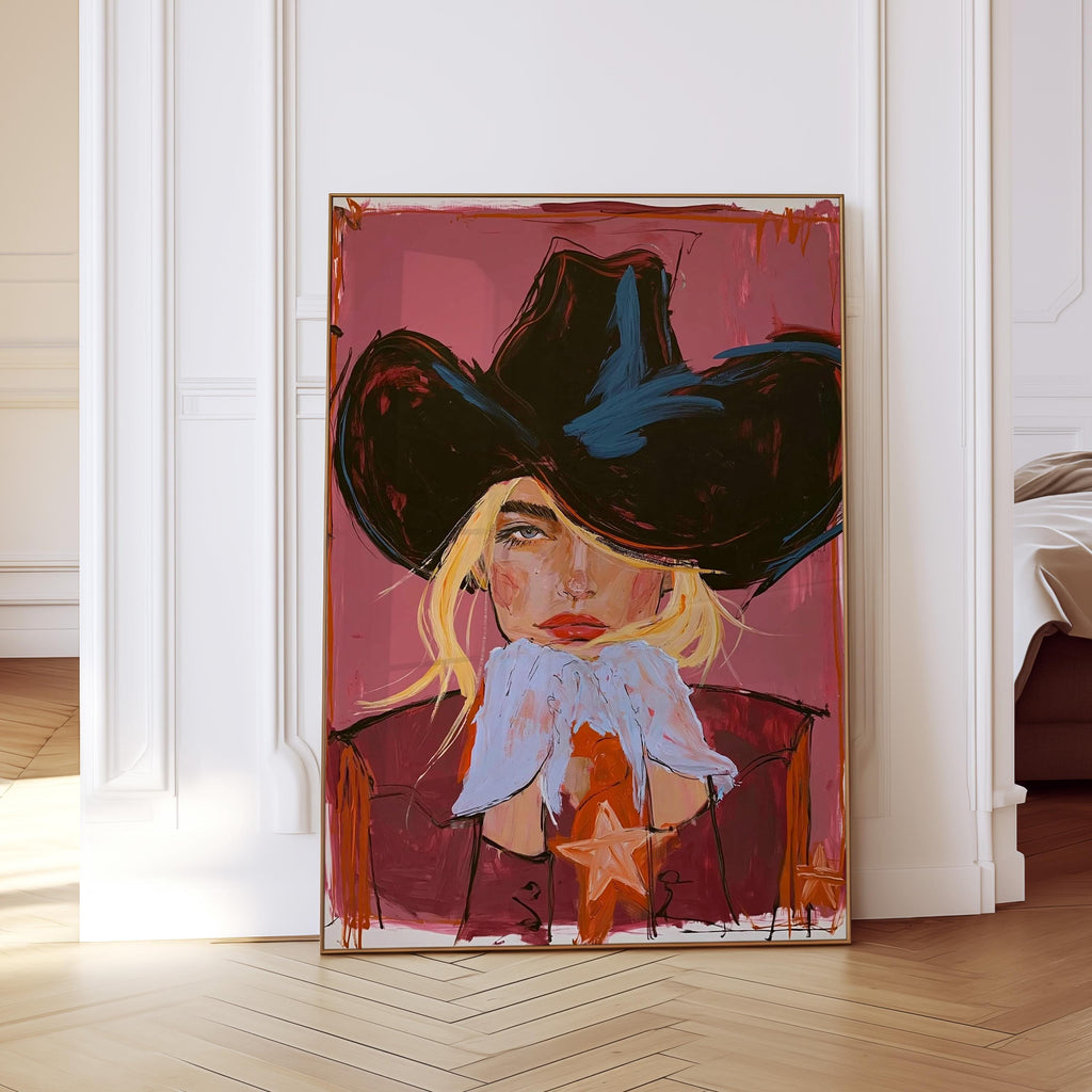 May include: Abstract portrait art print of a person wearing a black cowboy hat. The artwork features a person with blonde hair, red lips, and a maroon jacket with a star. The background is a shade of pink.