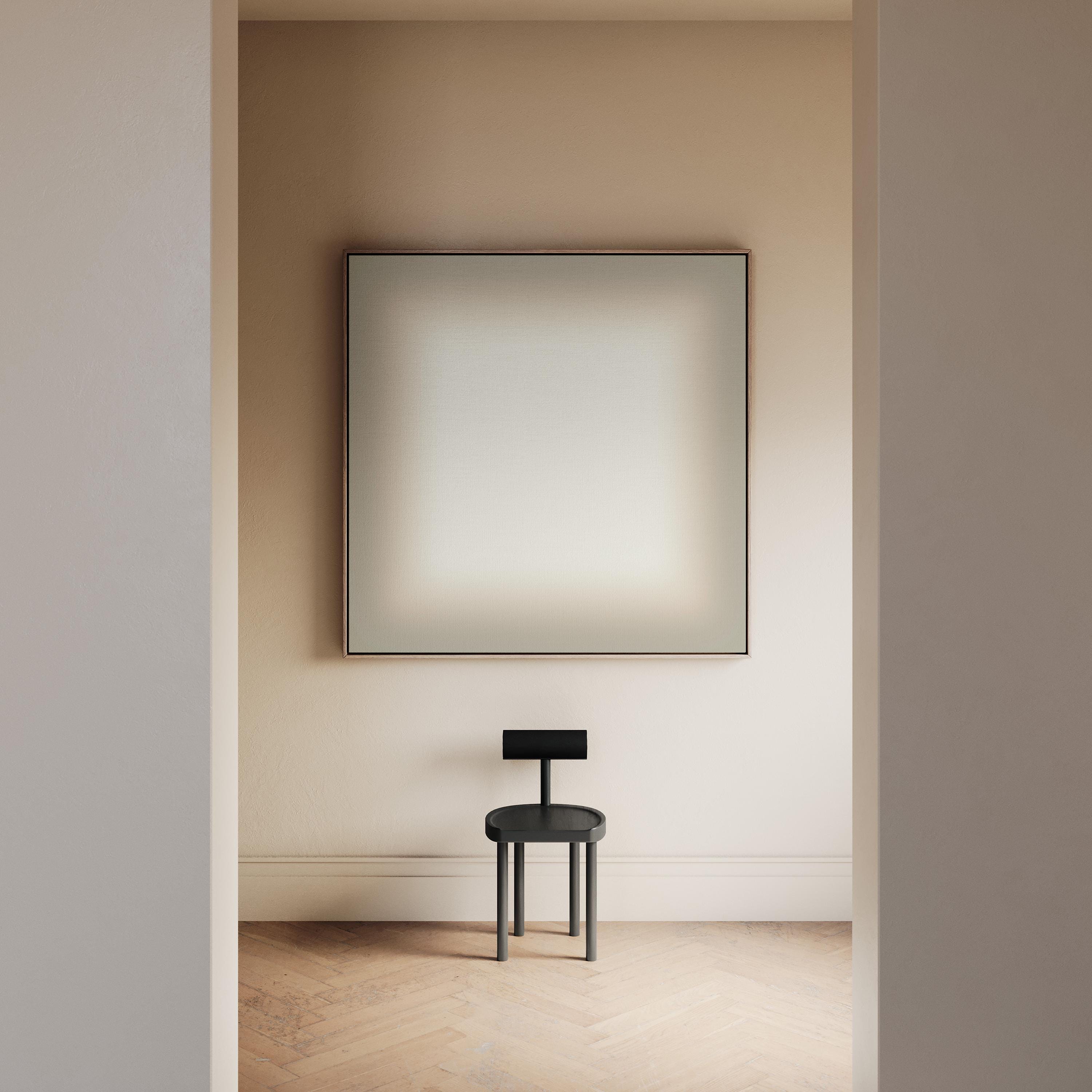 May include: A minimalist interior scene featuring a large, square artwork with a soft, gradient color scheme. Below, a small, dark gray chair with a circular seat and a rectangular backrest stands on a light-colored wooden floor.