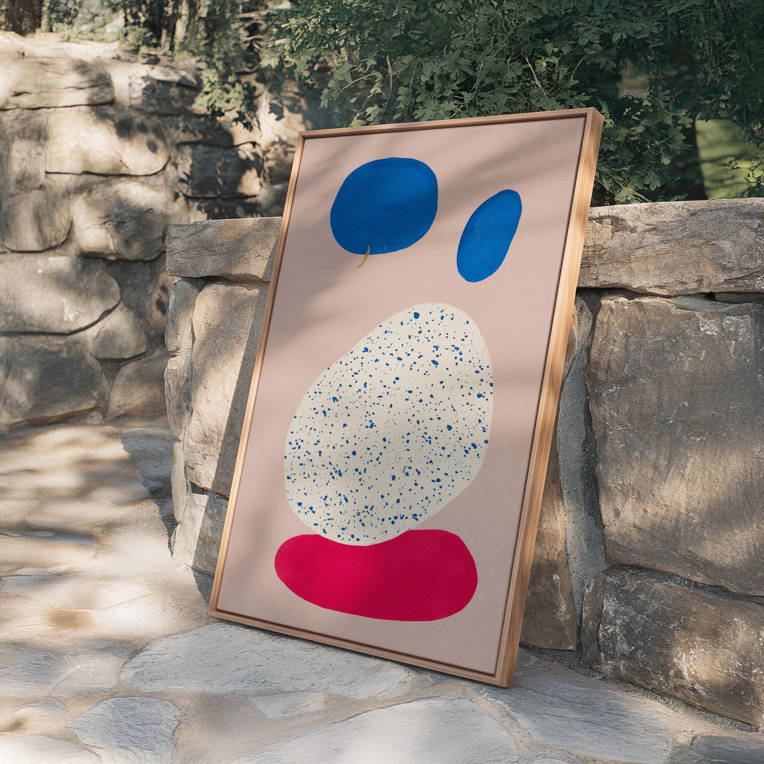 May include: Abstract art print featuring a light pink background with blue and red organic shapes. The largest shape is white with blue speckles. The artwork is framed in a natural wood frame.