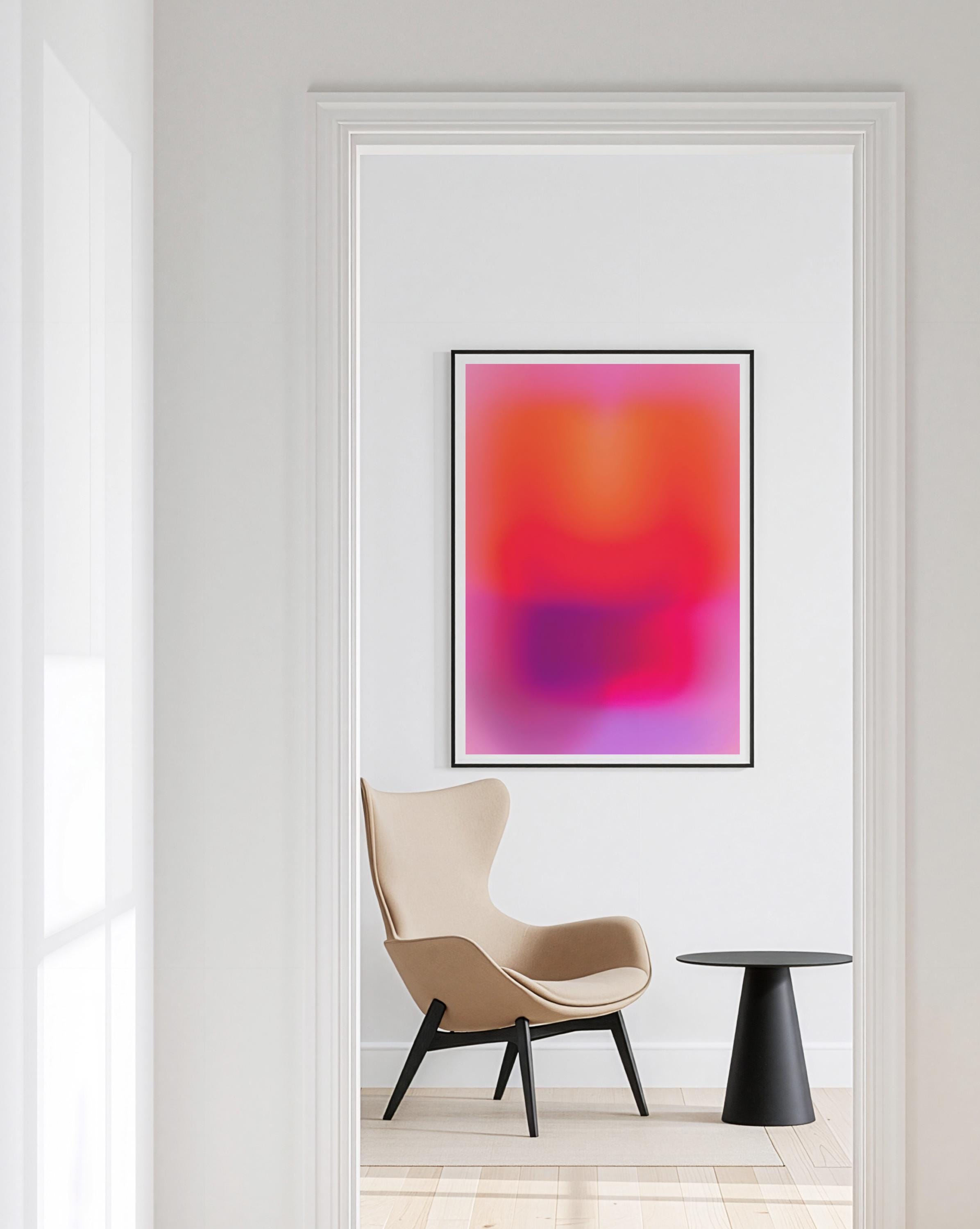 May include: A framed abstract art print with a vibrant gradient of pink, orange, and purple hues. The artwork is displayed in a black frame, hanging on a white wall. A beige armchair and a black side table are in the foreground.