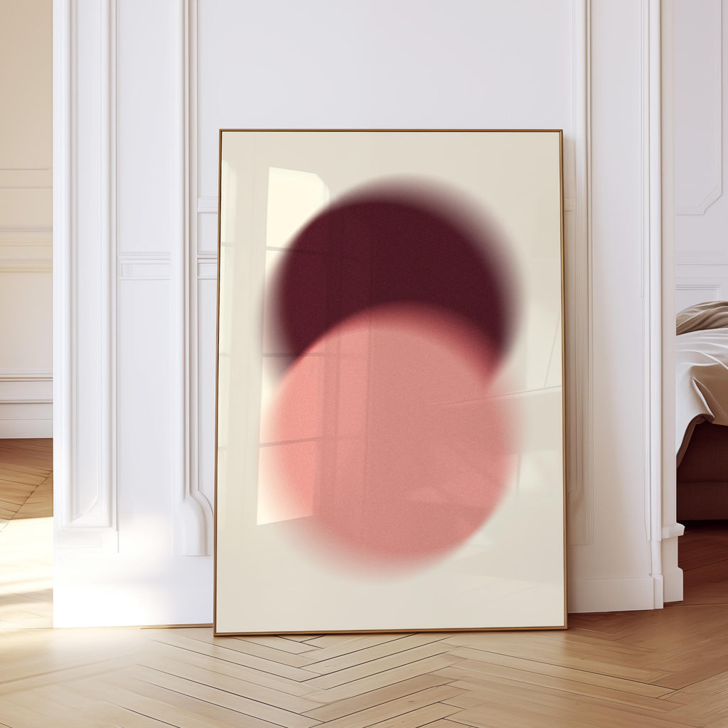 May include: Framed abstract art print featuring two overlapping blurred circles in shades of burgundy and coral pink against a cream background. The artwork is displayed in a room with white trim and a wooden floor.