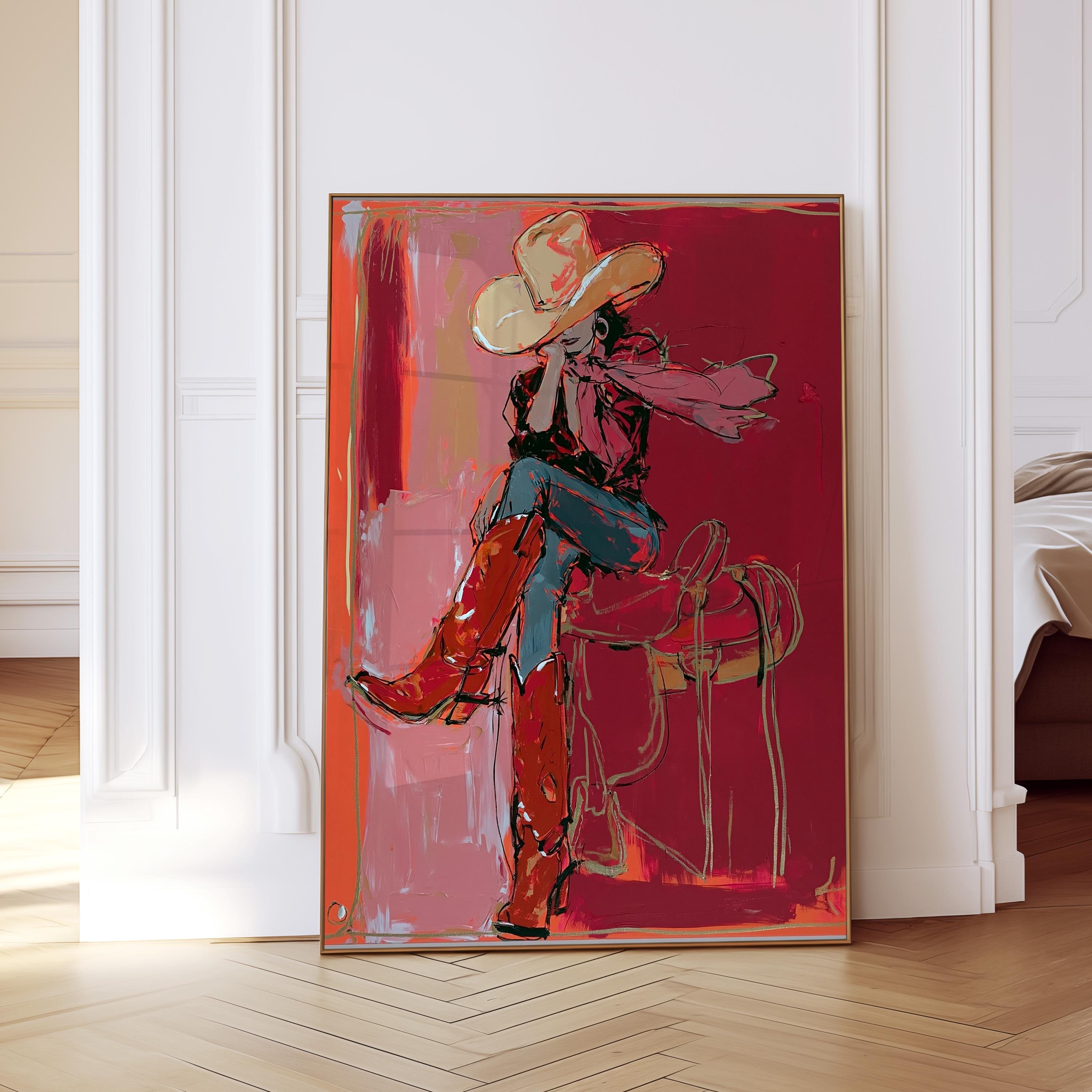 May include: Abstract art print of a person in a cowboy hat and boots, seated on a saddle. The artwork features a red and pink color palette with gold accents. The person is wearing a red shirt, blue jeans, and red boots.