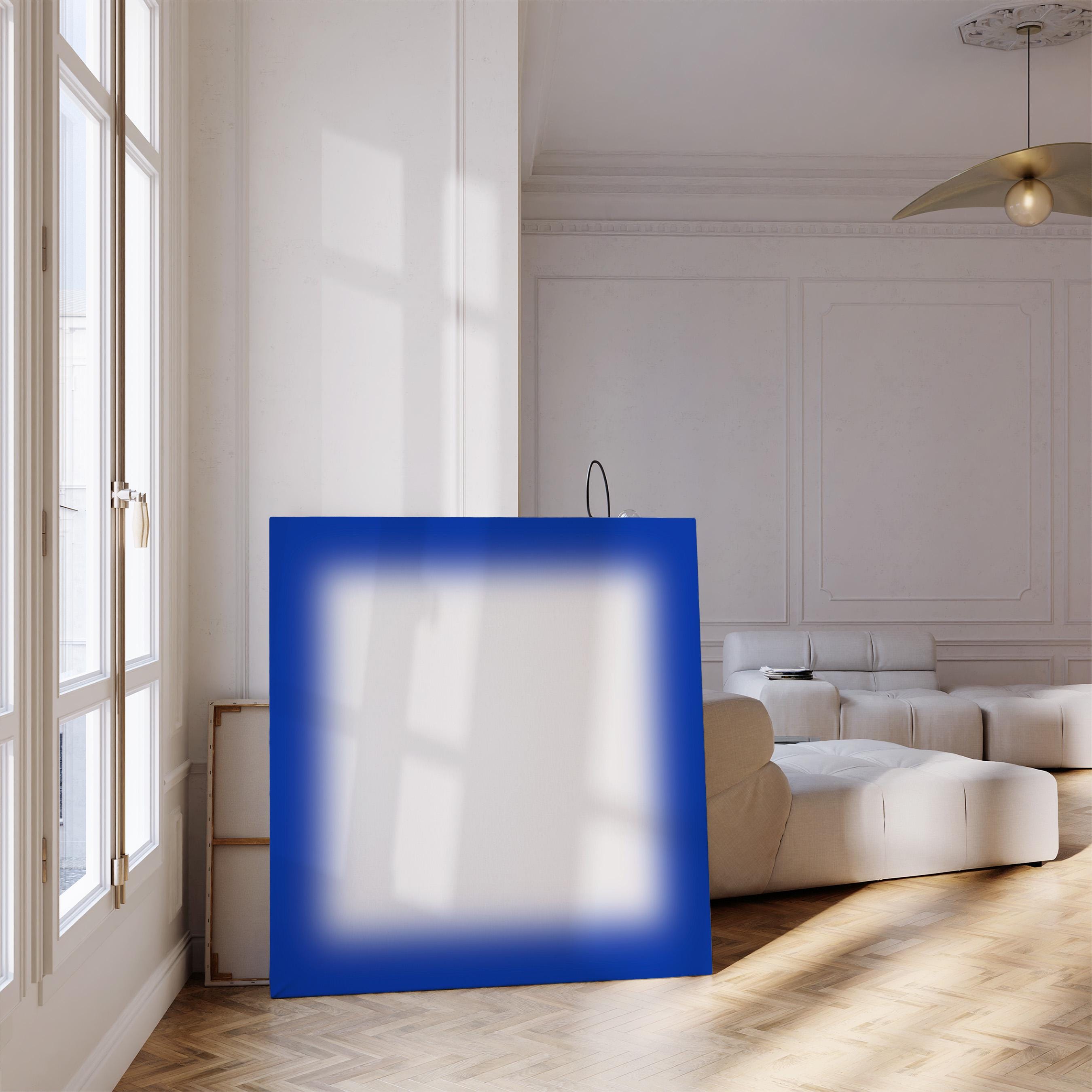 May include: A large, square canvas with a vibrant blue border and a white, blurred center. The artwork leans against a wall in a bright, modern room with a hardwood floor and a large window.