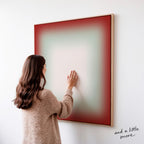 A woman in a brown sweater is standing in front of a large abstract painting, touching the frame of the artwork.