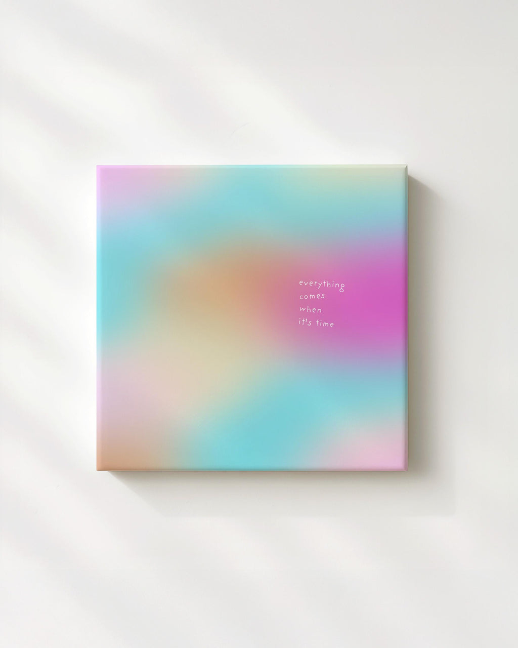 May include: A square canvas art piece with a soft, blurred background of pastel colors: turquoise, pink, orange, and yellow. The text "everything comes when it's time" is printed in a delicate, light font.