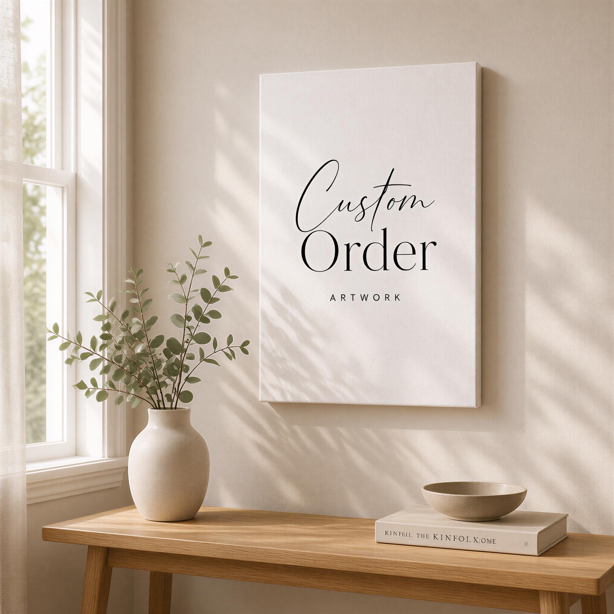 a wooden table with a vase of greenery, a book, and a bowl on it. Above the table, there is a white canvas with the text "Custom Order ARTWORK" written on it.