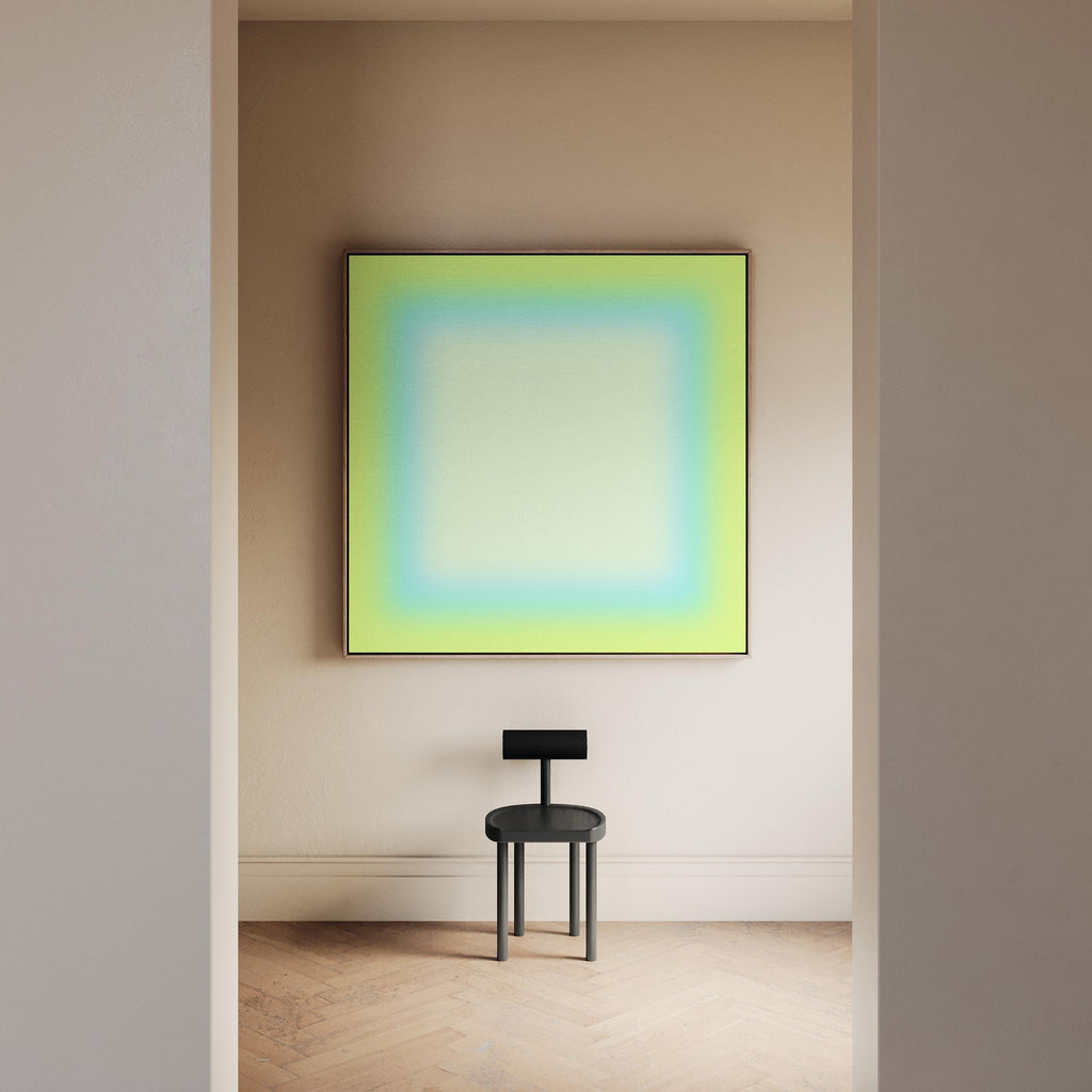 May include: A modern interior scene featuring a large square artwork with a gradient of green, blue, and white hues, framed in black. Below, a small, black chair with a circular seat and a rectangular backrest stands on a light-colored wooden floor.