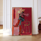 May include: Abstract art print of a person in a cowboy hat and boots, seated on a saddle. The artwork features a red and pink color palette with gold accents. The person is wearing a red shirt, blue jeans, and red boots.