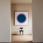 May include: A square wall art piece featuring a large, dark blue circular gradient centered on a pale pink background, displayed above a black stool with a flat, rectangular backrest and four cylindrical legs on a wooden floor.