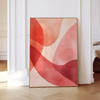 May include: Abstract art print featuring overlapping shapes in shades of red, pink, and peach. The artwork is framed in a thin gold frame and displayed in a room with white walls and a wooden floor. The art piece adds a modern touch to the interior.
