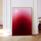 May include: A framed artwork with a gradient of colors from light pink to deep red. The artwork is displayed in a room with white trim and a wooden floor. The frame is a thin, gold color.