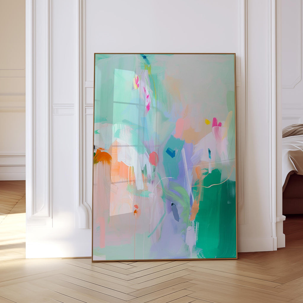 May include: Abstract art print with a gold frame. The artwork features a vibrant mix of colors, including green, blue, pink, and orange, with brushstrokes and splatters. The painting is displayed against a white wall and a light wood floor.