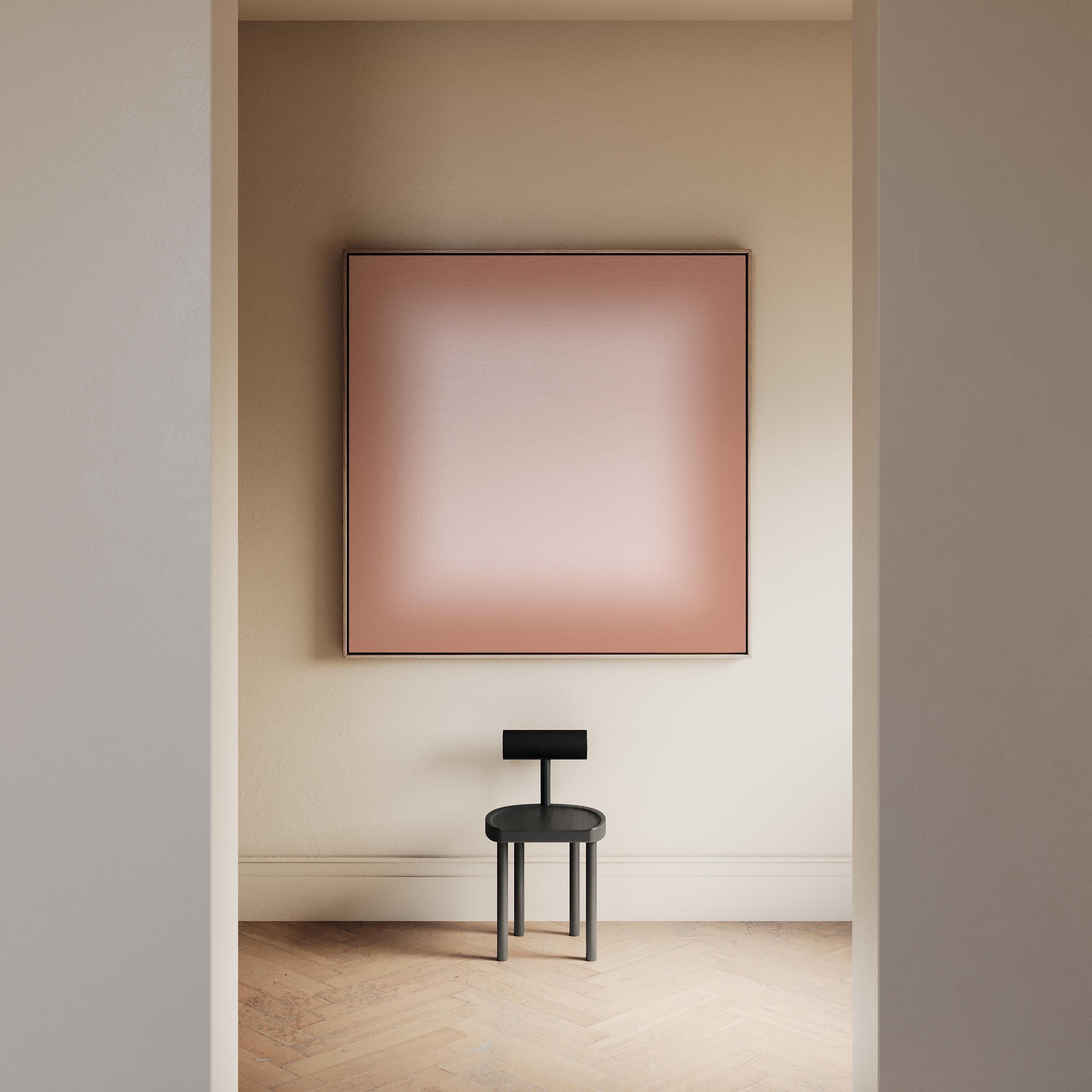 May include: A square wall art piece featuring a soft gradient from a dusty rose pink center to a darker terracotta border, framed in a thin dark edge. Below it sits a small black stool with a circular seat and a rectangular backrest.