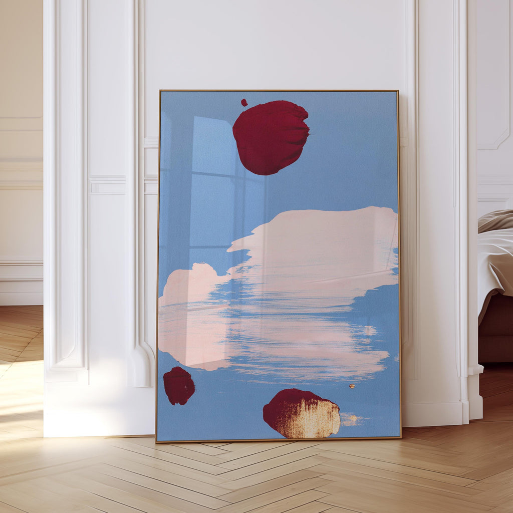 May include: Abstract art print featuring a light blue background with large brushstrokes of pink and white. Three maroon-colored shapes are scattered across the canvas. The artwork is framed in a thin, gold-colored frame.