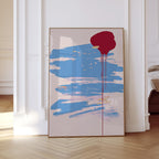 May include: Abstract art print featuring a large red shape with dripping paint over a light blue brushstroke design. The artwork is framed in a thin, gold-colored frame and is displayed against a white wall.